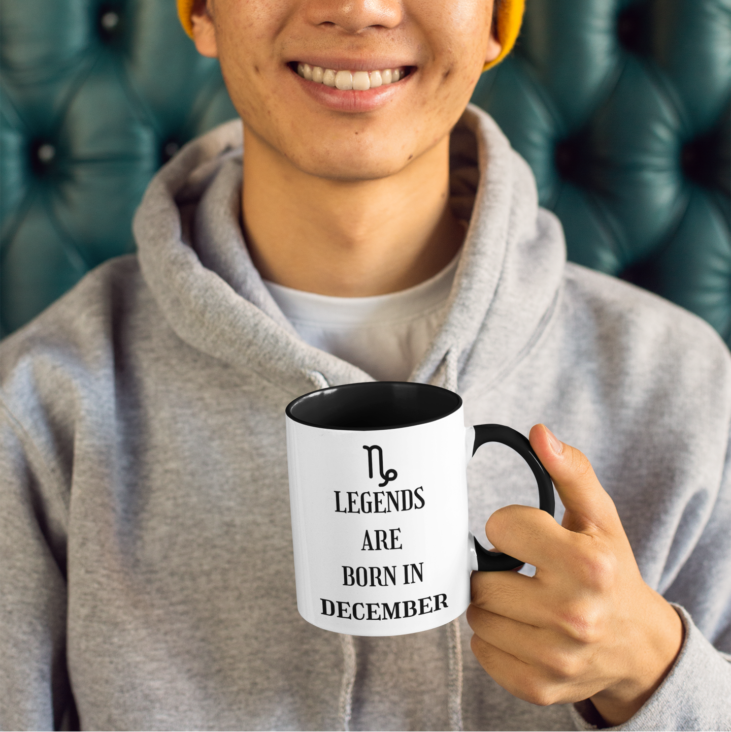 Person holding a mug with 'Legends are born in December' text, wearing a yellow beanie and gray hoodie.