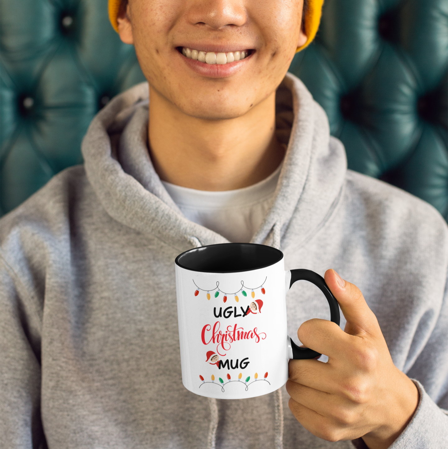 Person holding a mug with humorous text and graphics, wearing a yellow beanie and gray hoodie.