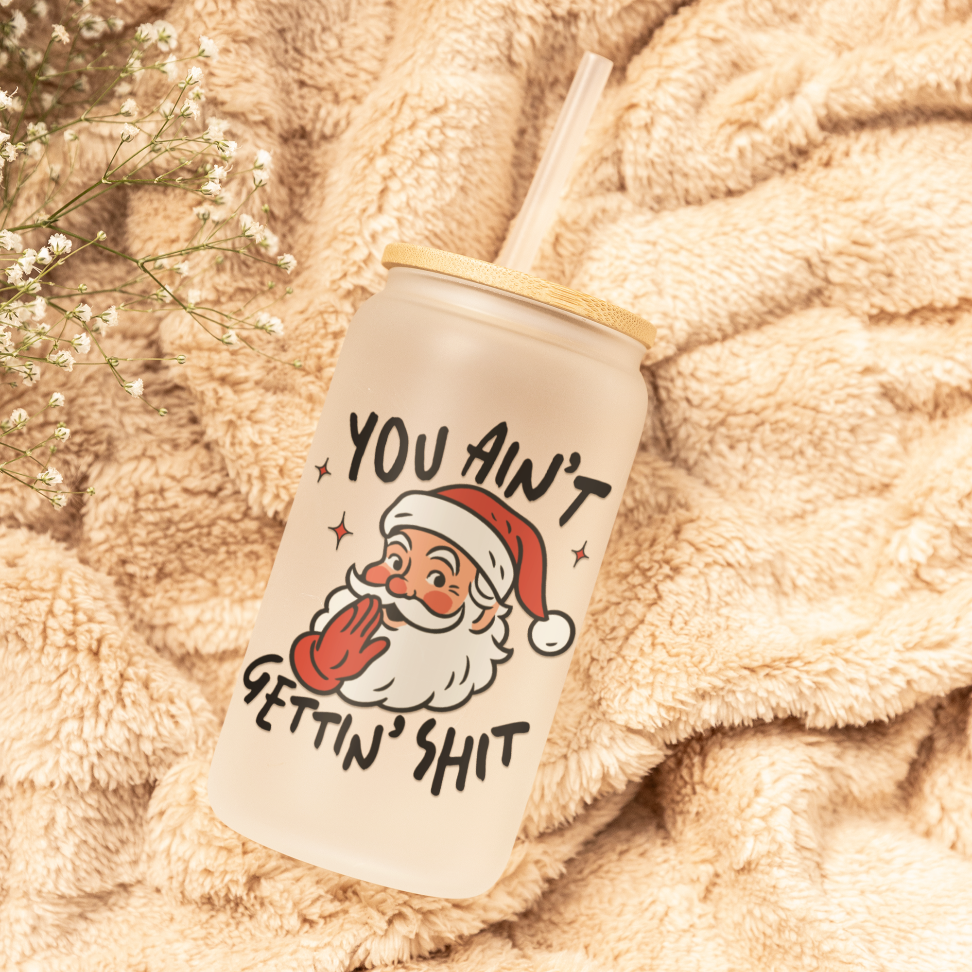 Tumbler with Santa Claus graphic and text on a soft, beige blanket