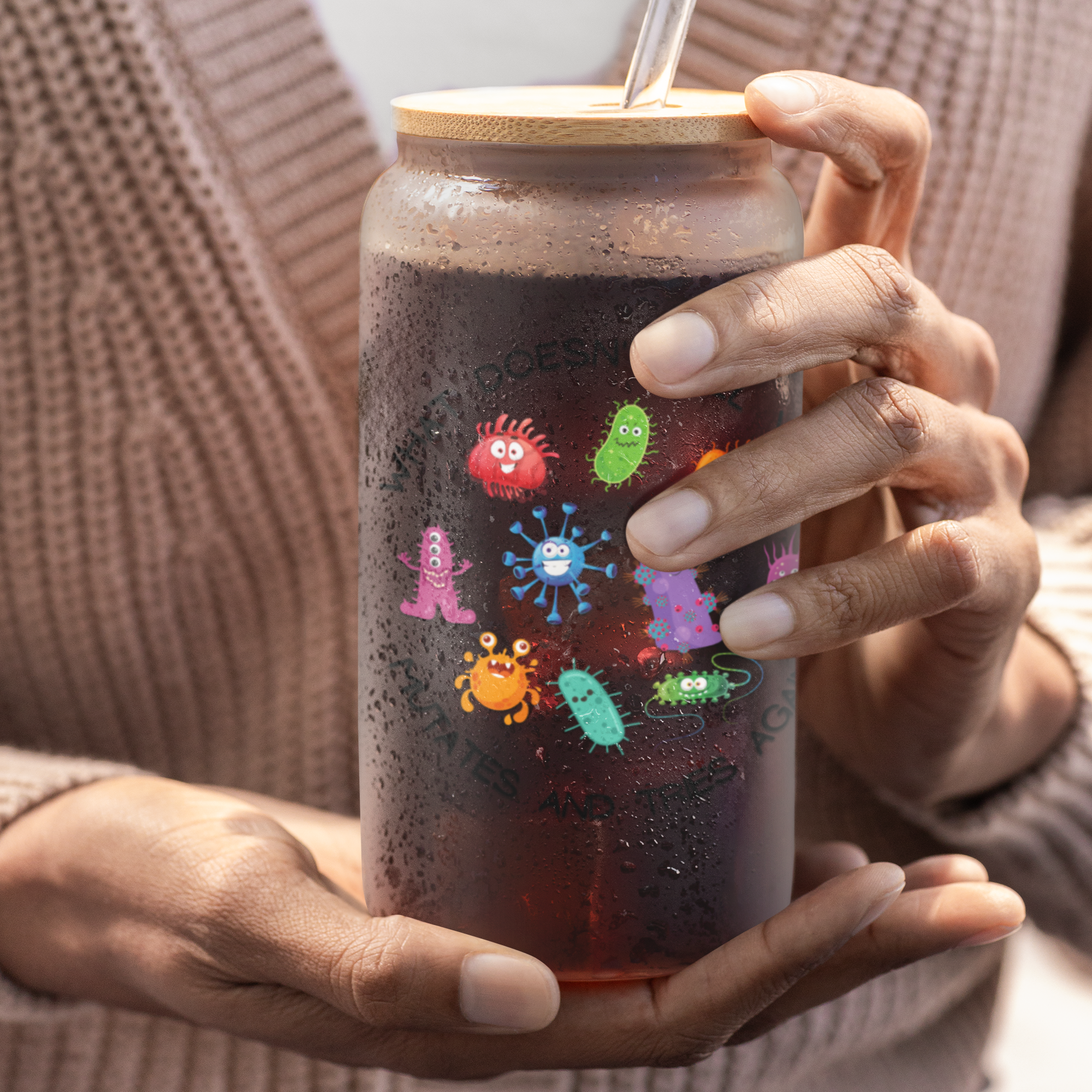 Person holding a jar with colorful (microbe) illustrations on a dark liquid.