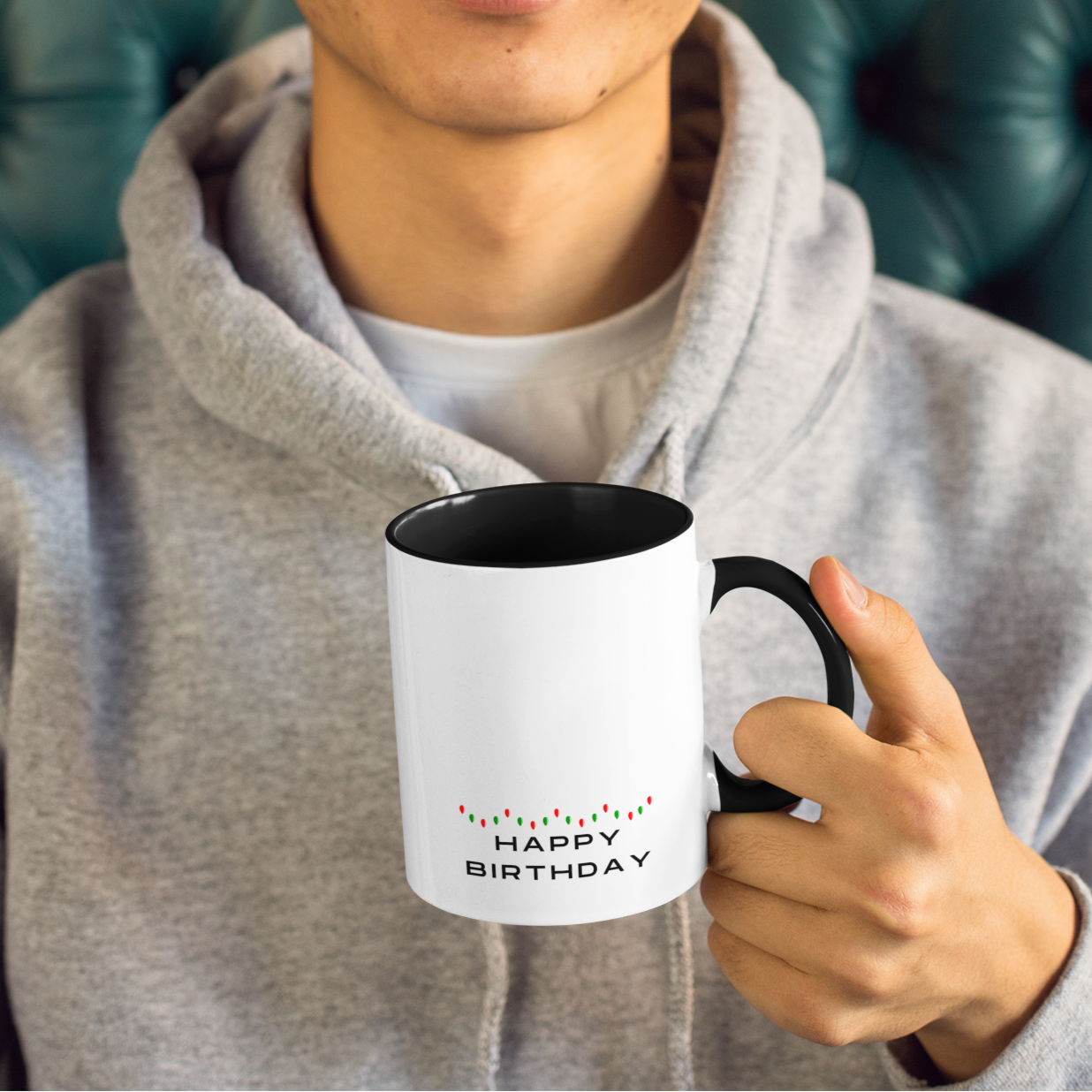 Person wearing a yellow beanie and gray hoodie holding a mug with 'Happy Birthday' text.