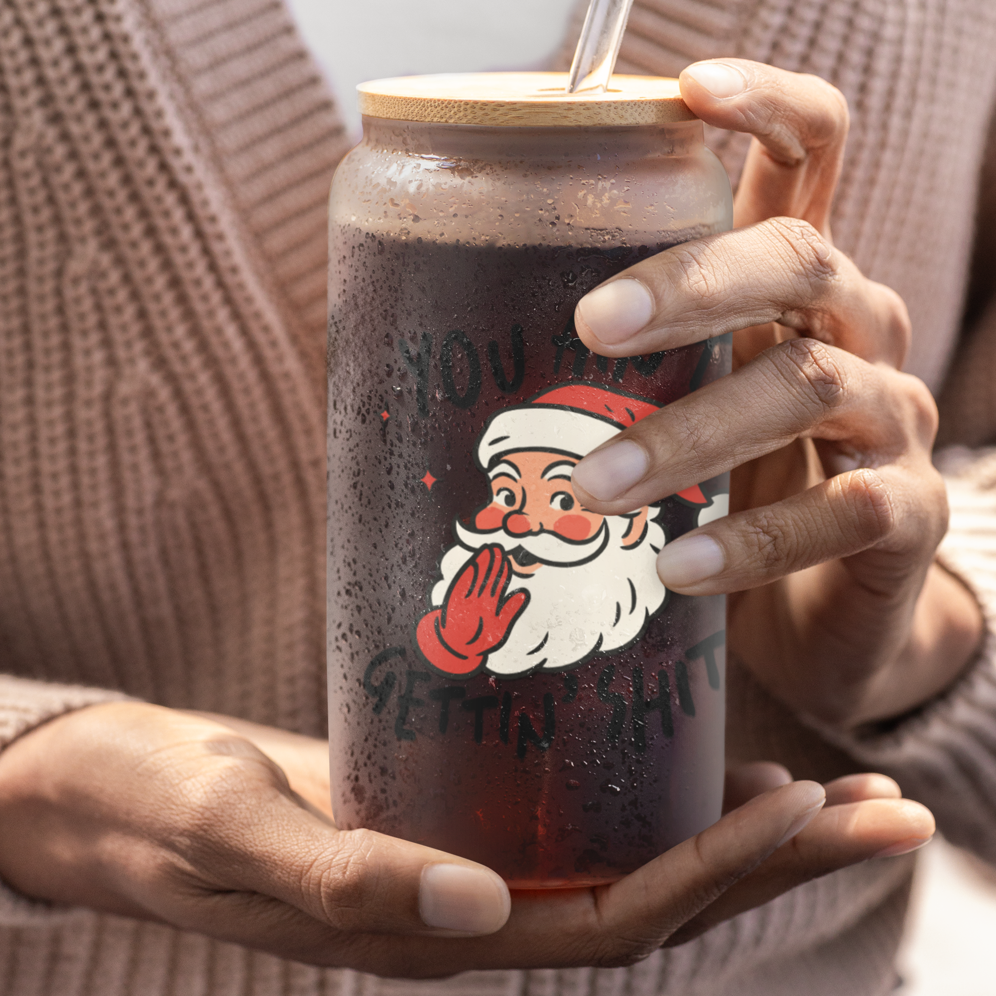 Person holding a tumbler with a Santa Claus design and wooden lid.