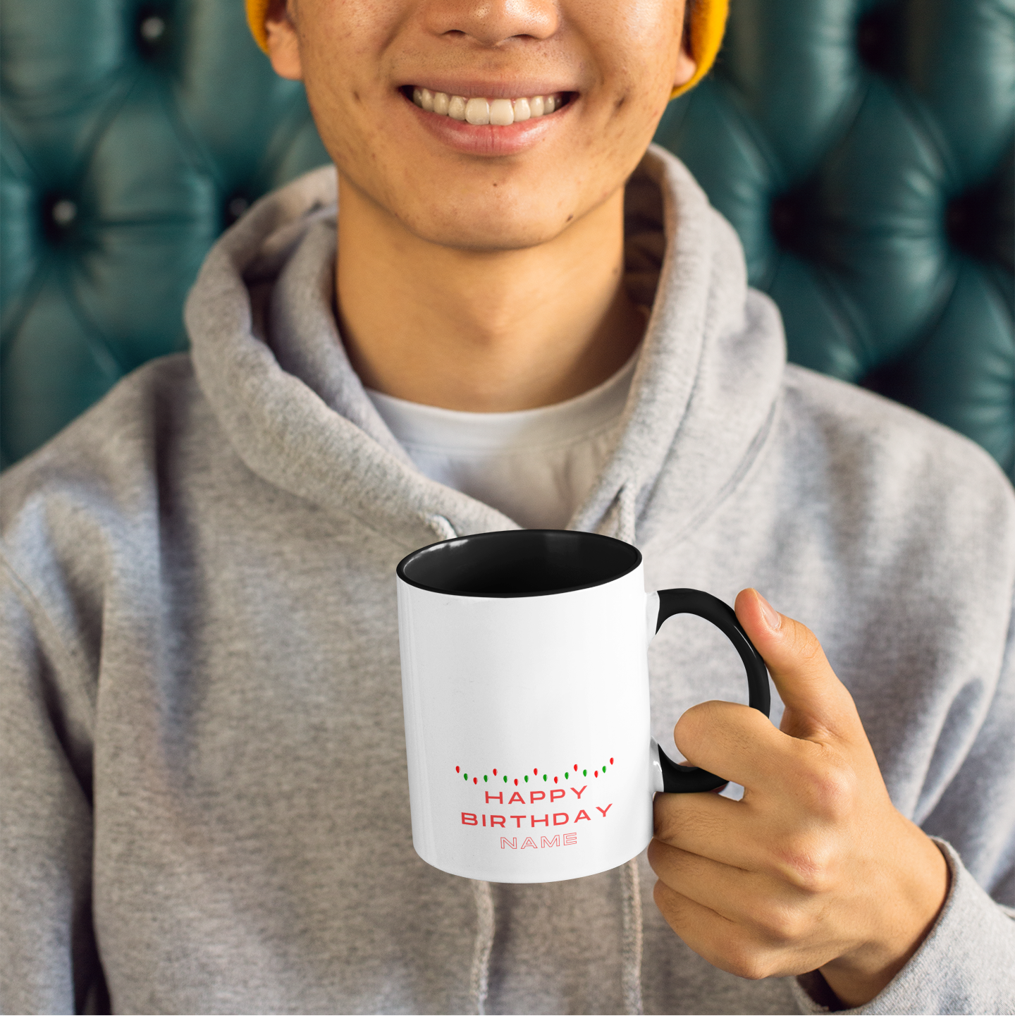 Person wearing a yellow beanie and gray hoodie holding a mug with 'Happy Birthday' text.