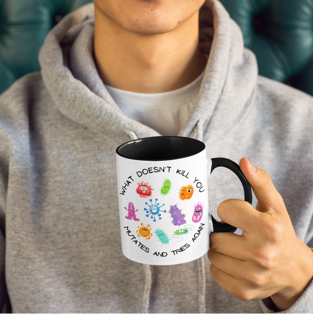 Person holding a mug with colorful designs and text, wearing a yellow beanie and gray hoodie.