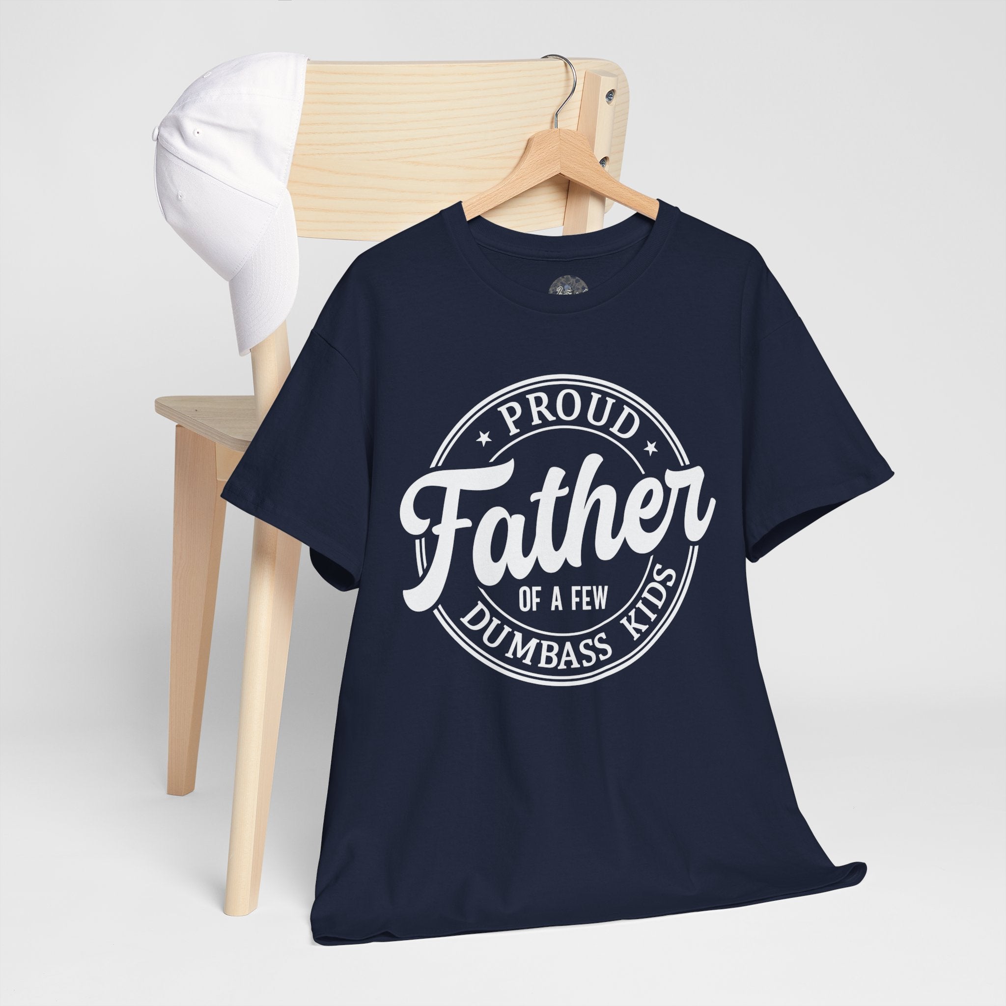 Navy blue t-shirt with Proud Father Of A Few Dumbass Kids text on a wooden chair against a white background