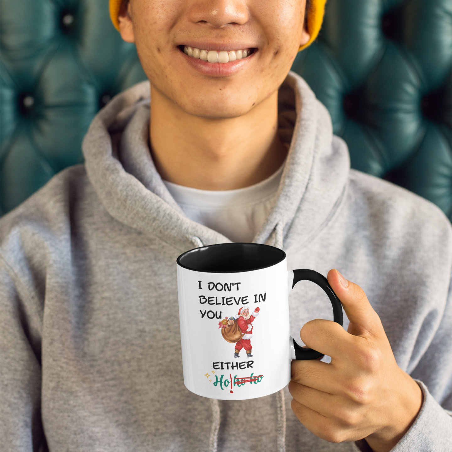 Person holding a mug with humorous text and graphics, wearing a yellow beanie and gray hoodie.