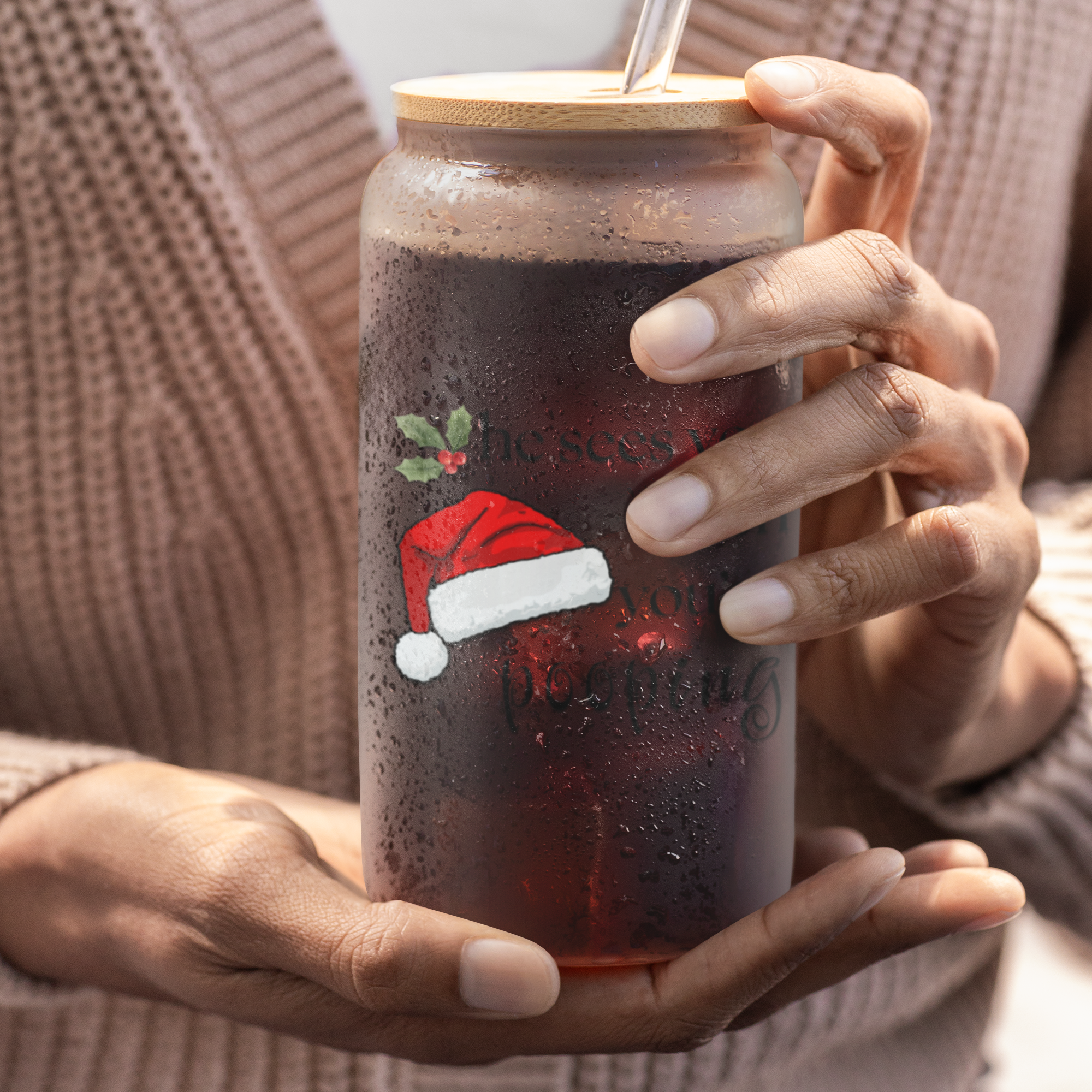 Person holding a frosted glass with a sarcastic christmas design, wearing a beige sweater.