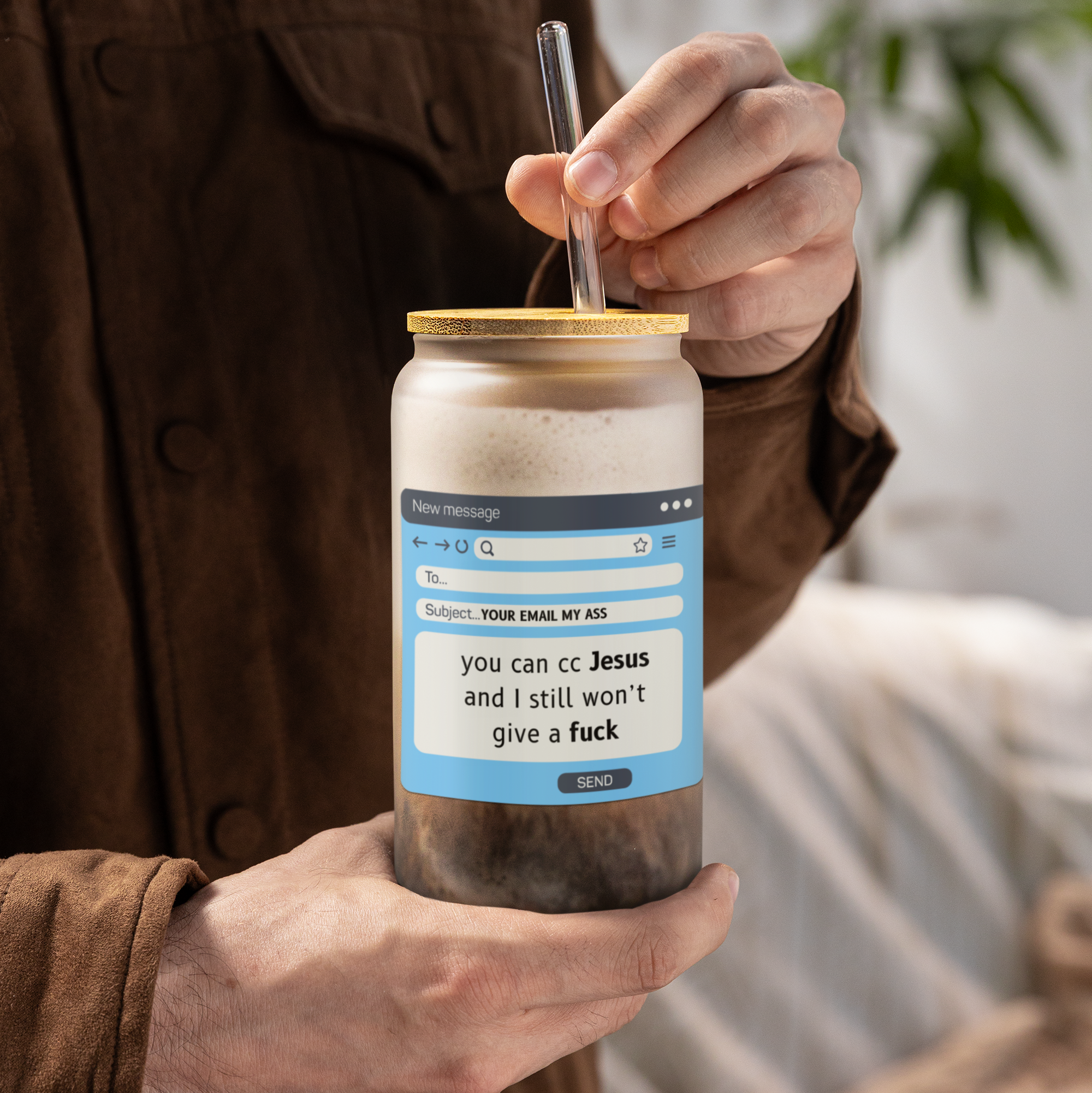Person holding a frosted glass iced coffee cup with a humorous label and straw, blurred background